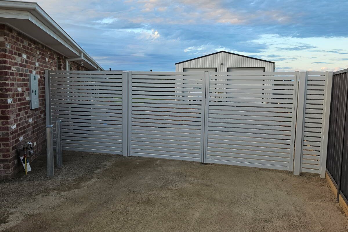 Light grey slatted driveway gate between brick and metal fences
